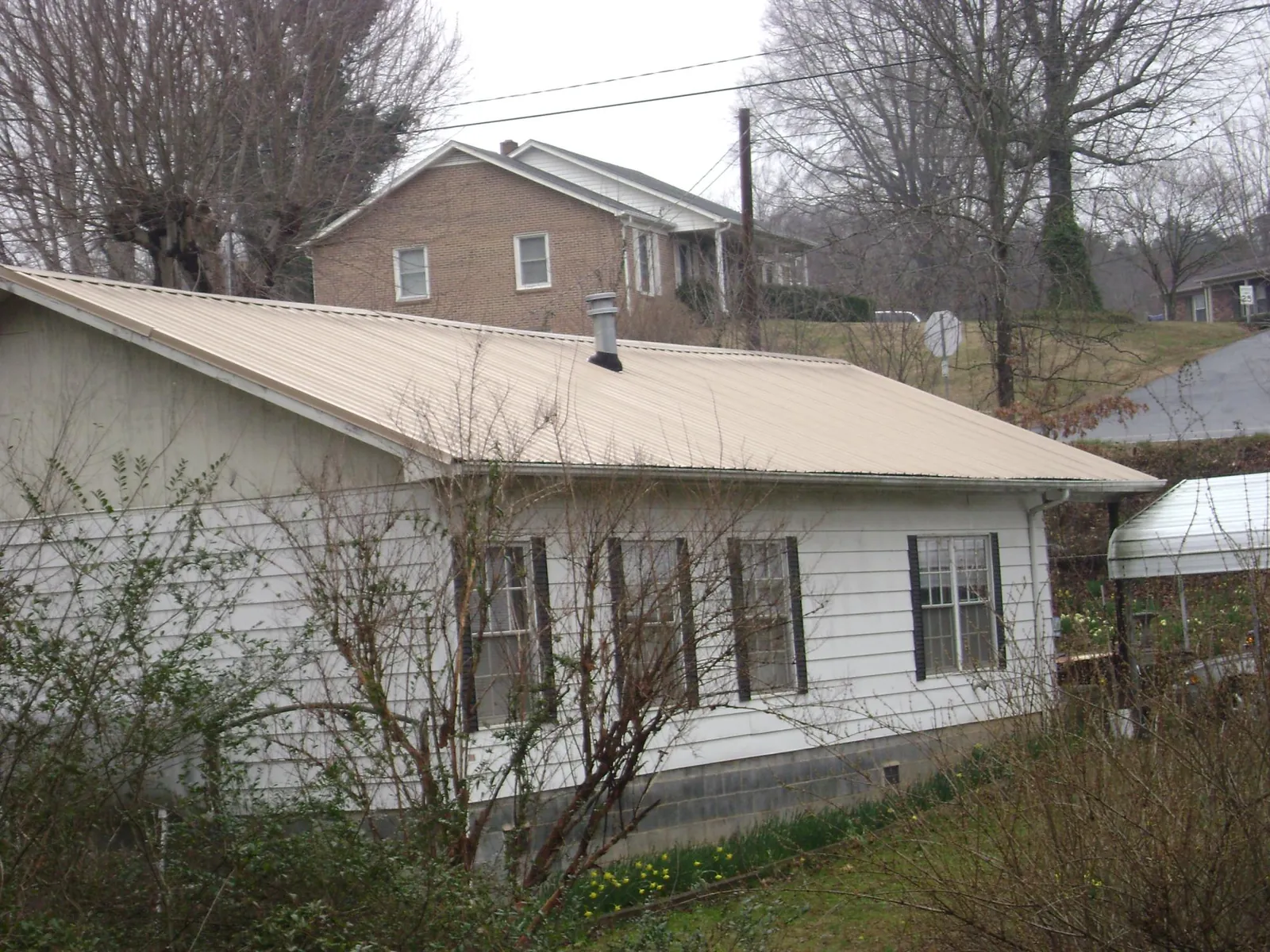 Tan metal roof on a white sided house set into a hillside — Commercial Roofing by Roofing Brothers in Swansea