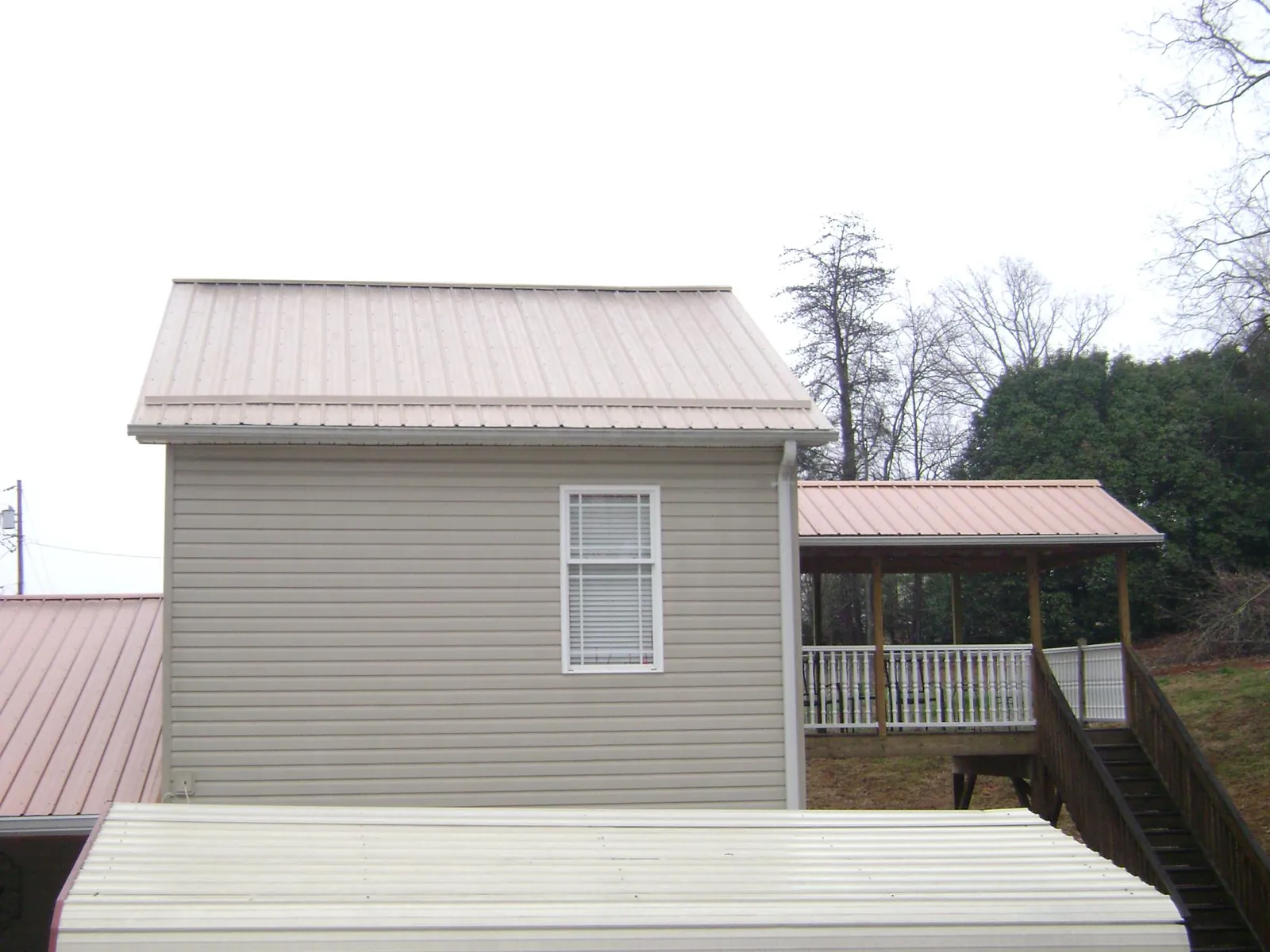 Tan metal roofs on a two story addition and attached porch, from a Roof Replacement job in Swansea